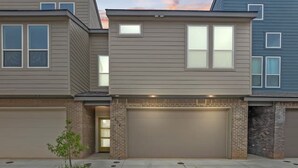 Un immeuble résidentiel moderne à deux étages, doté d’un garage, d’un petit jardin et offrant une vue sur un ciel dégagé.