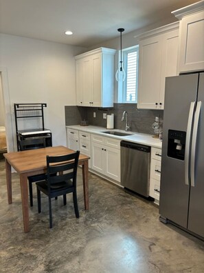 A kitchen with white cabinets, a stainless steel refrigerator, a wooden dining table, and a black chair.