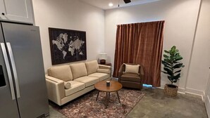 Ein modernes Wohnzimmer mit einem beigen Sofa, einem Couchtisch, einer Stehlampe, einer Weltkarte als Kunstwerk, einem Deckenventilator und einem Blumentopf.