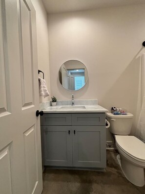 Un baño con un lavamanos blanco, un espejo redondo y un inodoro.