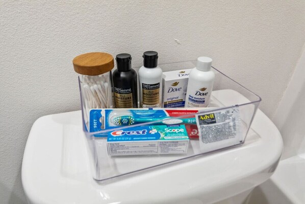 A clear plastic organizer on a toilet holding various toiletries including Crest toothpaste, Dove soap, and other personal care items.