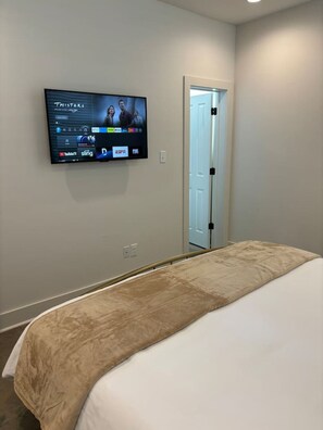 A hotel room with a bed, a TV mounted on the wall displaying various channels, and a door leading to another room.