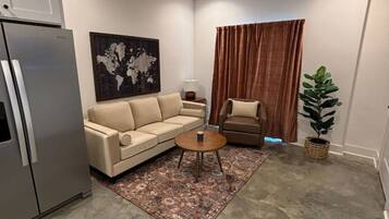 Un salon moderne avec un canapé beige, une table basse, un lampadaire, une œuvre d’art représentant une carte du monde, un ventilateur de plafond et une plante en pot.