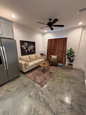 A modern living room with a beige sofa, a coffee table, a floor lamp, a world map artwork, a ceiling fan, and a potted plant.
