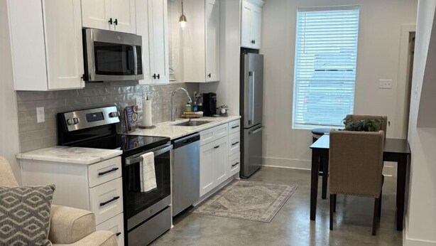 A modern kitchen with white cabinets, stainless steel appliances, and a dining area with a table and chairs. - NEW-Beignet House-Luxe Mattress-Fast WiFi-Book Now (Lafayette)