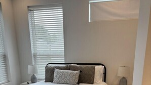 A bedroom with a bed, bedside tables, a rug, and a window with blinds. - NEW-Beignet House-Luxe Mattress-Fast WiFi-Book Now (Lafayette)