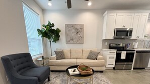 A modern living room with a dark armchair, a beige sofa, and a coffee table with a basket. A large plant is beside the sofa, and a painting hangs on the wall. - NEW-Beignet House-Luxe Mattress-Fast WiFi-Book Now (Lafayette)