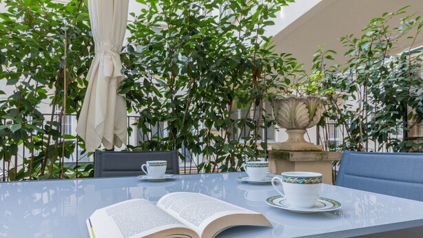 An outdoor table with a book, two cups, and saucers, surrounded by greenery and a stone fountain. - Prestige Apartment Via Roma by Wonderful Italy (Torino)