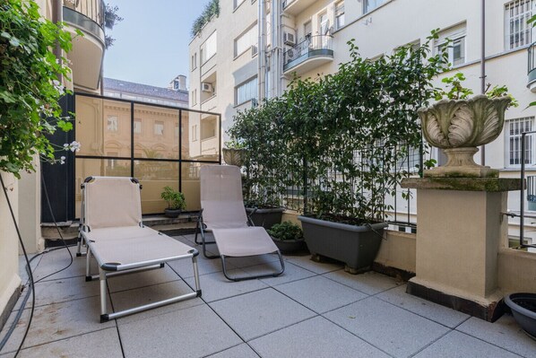 Una terraza en la azotea con dos sillones de descanso, plantas en macetas y una urna decorativa.