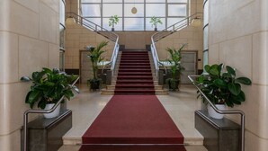 A grand staircase with a red carpet, flanked by potted plants, leading to a high ceiling with large windows. - Prestige Apartment Via Roma by Wonderful Italy (Torino)
