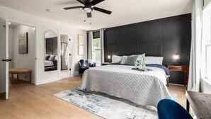 Ein Schlafzimmer mit Bett, Deckenventilator, Nachttisch, Stuhl, Bank und einem großen Fenster.