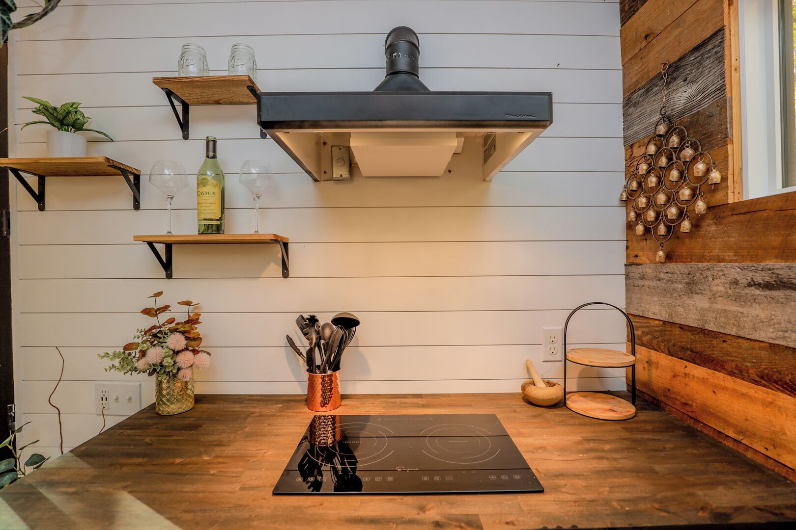 A kitchen with wooden shelves, a built-in stove, and a hanging bell decoration.