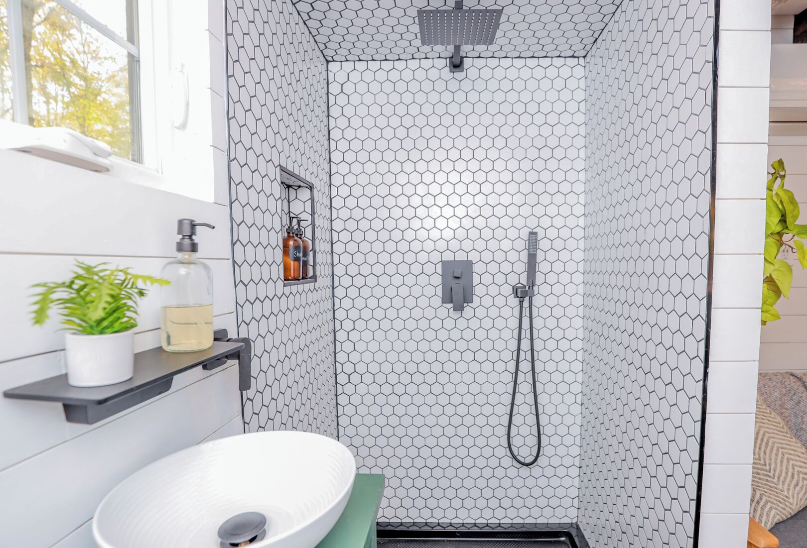 A bathroom with a white sink, a shower with a hexagonal tile pattern, and a window with a view of trees.