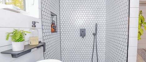 A bathroom with a white sink, a shower with a hexagonal tile pattern, and a window with a view of trees.