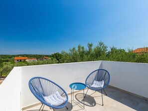 A rooftop terrace with two blue wire-framed chairs and a small blue table, overlooking a landscape with buildings and greenery. - Adorable Home With Private Garden and Bubble Bath (Marcana)