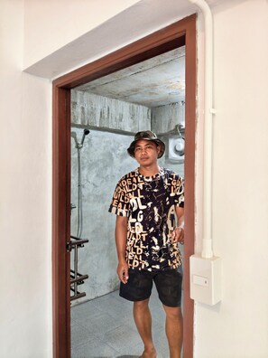 A person standing in a doorway with a concrete wall and a shower in the background. - GJ TOUR and HOME STAY (Pangmapha)
