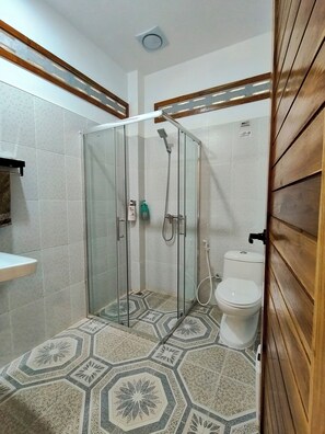 Een douche met glazen deur, toilet en vloertegels met patroon.