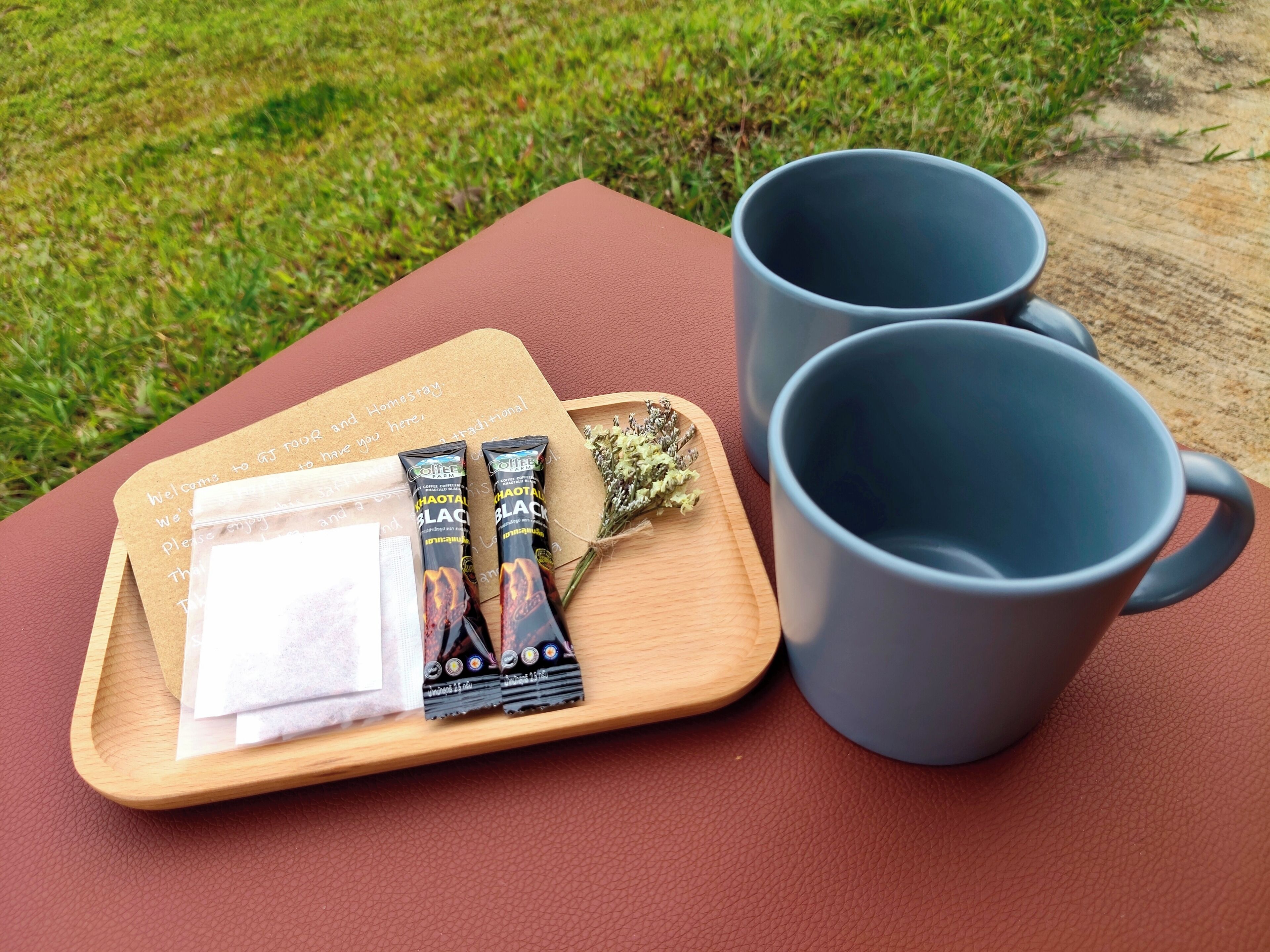 Un plateau en bois sur lequel reposent deux sachets de thé chai, un petit bouquet et deux tasses grises, le tout posé sur une surface marron.