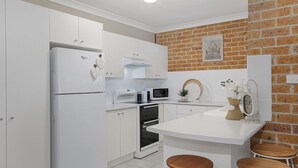 A modern kitchen with white cabinetry, a brick wall, a microwave, a stove, and a small island with stools. - Jervis Joy – child friendly coastal retreat (Callala Beach)