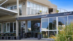 A two-story building with a cafe named "Calabrissa Sella" on the ground floor. There are outdoor seating areas with tables and chairs. - Jervis Joy – child friendly coastal retreat (Callala Beach)