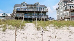A beachfront property with a multi-story building, wooden walkways, and a sandy beach. - Surfer's Delight - Amazing 6 BR Oceanfront Home in Hampton Colony (North Topsail Beach)