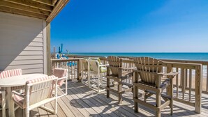 A wooden deck with outdoor furniture, including chairs and a table, overlooking a beach. - Son Burn - 3BR Oceanfront Turtle Cove Townhouse (Surf City)