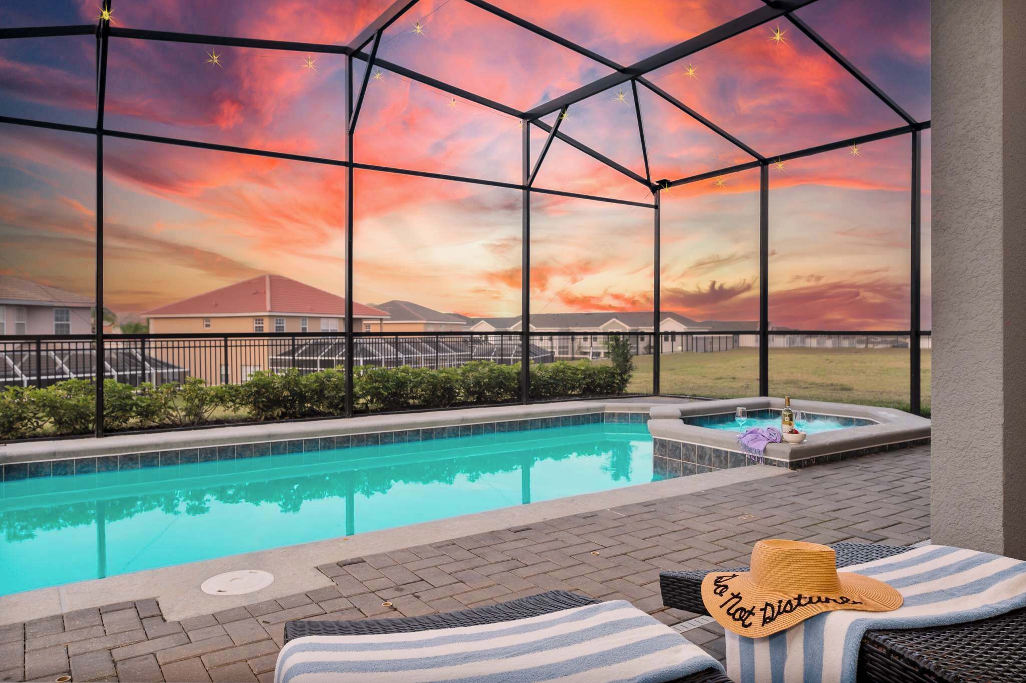 Ein Poolbereich mit Whirlpool, Liegestühlen und Blick auf den Sonnenuntergang durch eine Glaskonstruktion.