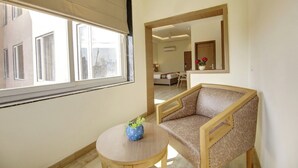 A room with a large window, a round table with a vase, a sofa, and a mirror reflecting the room. - Buddha Residency Sravasti by DD (Ikauna)