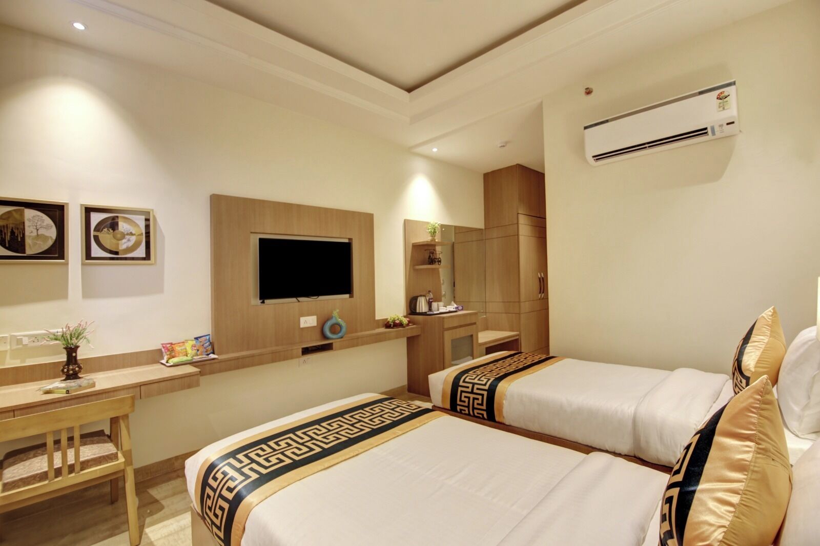 A hotel room with two beds, a desk, a television, and an air conditioning unit.