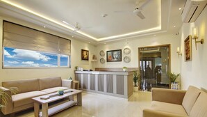 A modern hotel lobby with a reception desk, sofas, a coffee table, and a large window with a view of the sky. - Buddha Residency Sravasti by DD (Ikauna)