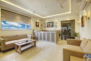 A modern hotel lobby with a reception desk, sofas, a coffee table, and a large window with a view of the sky.