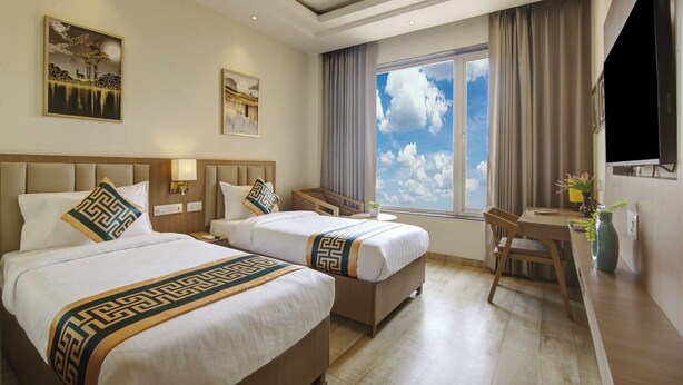A hotel room with two beds, a desk, a chair, a TV, and a large window with a view of the sky. - Buddha Residency Sravasti by DD (Ikauna)