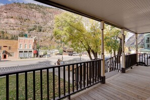 A wooden deck with a black railing overlooking a street with buildings and a mountain in the background. - Patio & Mountain Views: Central Ouray Getaway! (Ouray)