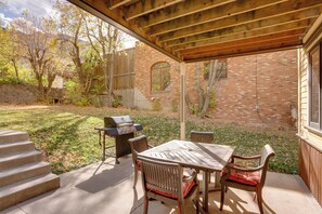 An outdoor patio with a wooden table and chairs, a barbecue grill, and a brick building in the background. - Patio & Mountain Views: Central Ouray Getaway! (Ouray)