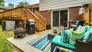 Een achtertuin met een houten terras, een barbecue, een vuurkorf, tuinmeubilair en een patio.