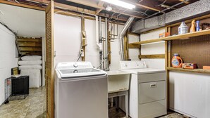 Een wasserette met opgestapelde lakens, een wasmachine, een droger en een prikbord met schoonmaakmiddelen.