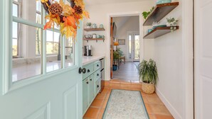 A kitchen with teal cabinetry, a window with a view, and a hallway leading to a dining area. - Steps to Sutter Creek: Chic Wine Country Cottage (Sutter Creek)