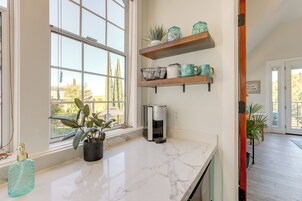 Una cocina con encimera de mármol, cafetera y estantes con utensilios de cocina.