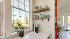 A kitchen with a marble countertop, a coffee maker, and shelves with kitchenware. - Steps to Sutter Creek: Chic Wine Country Cottage (Sutter Creek)