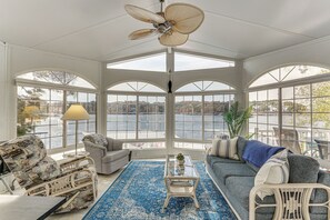 A sunroom with a large arched window overlooking a body of water, a ceiling fan, and a blue patterned rug. - Fireplace, Deck & Grill: Lake Ozark Family Retreat (Lake Ozark)