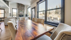 A spacious room with a large wooden dining table surrounded by chairs, a stone fireplace, and large windows offering a view of a snowy landscape. - 8 Mi to Keystone Resort: Mtn-view Townhome (Silverthorne)
