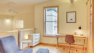 A modern room with a desk, two chairs, a small side table, a lamp, and a ceiling fan.