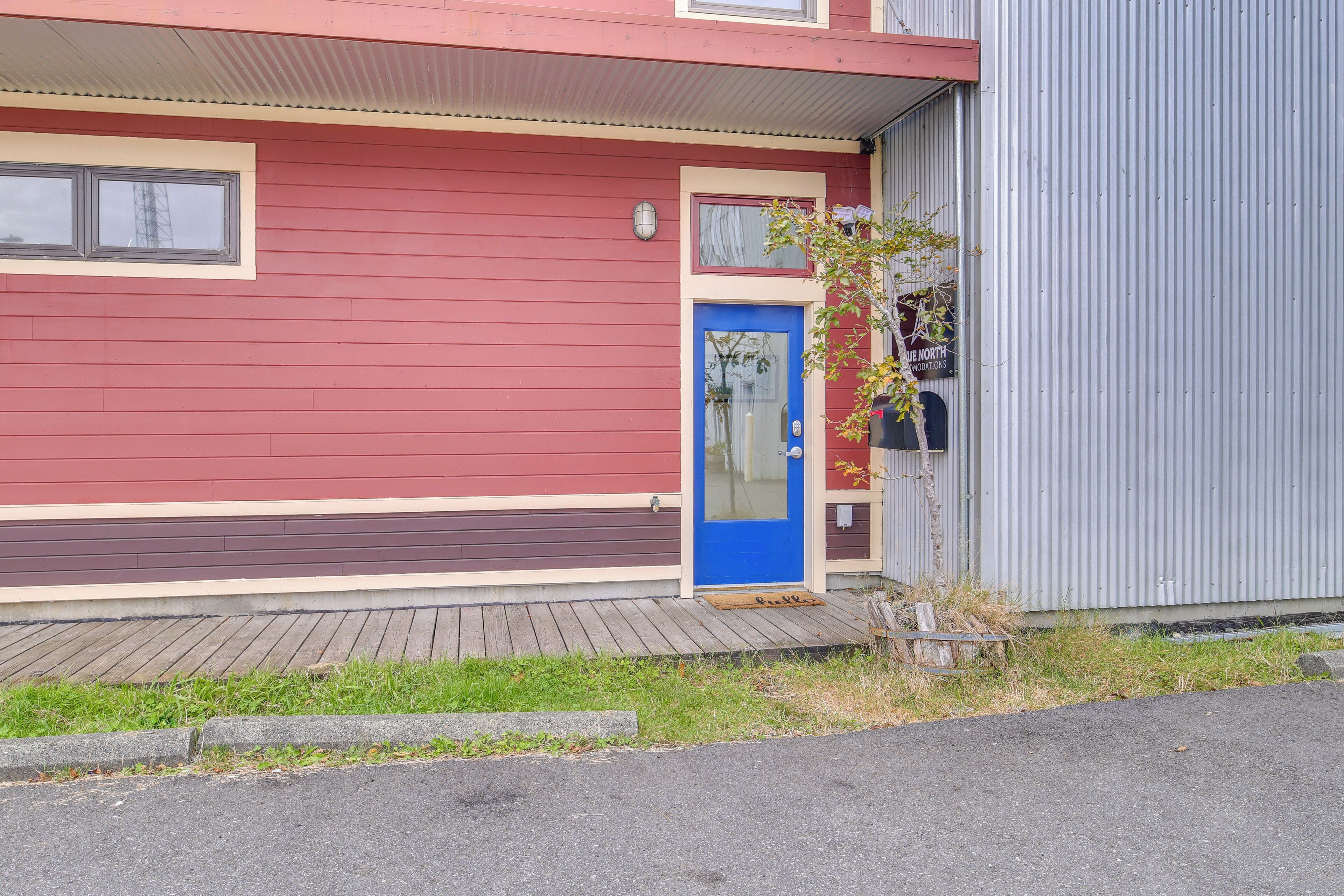A red building with a blue door, a small porch, and a metal structure to the right.