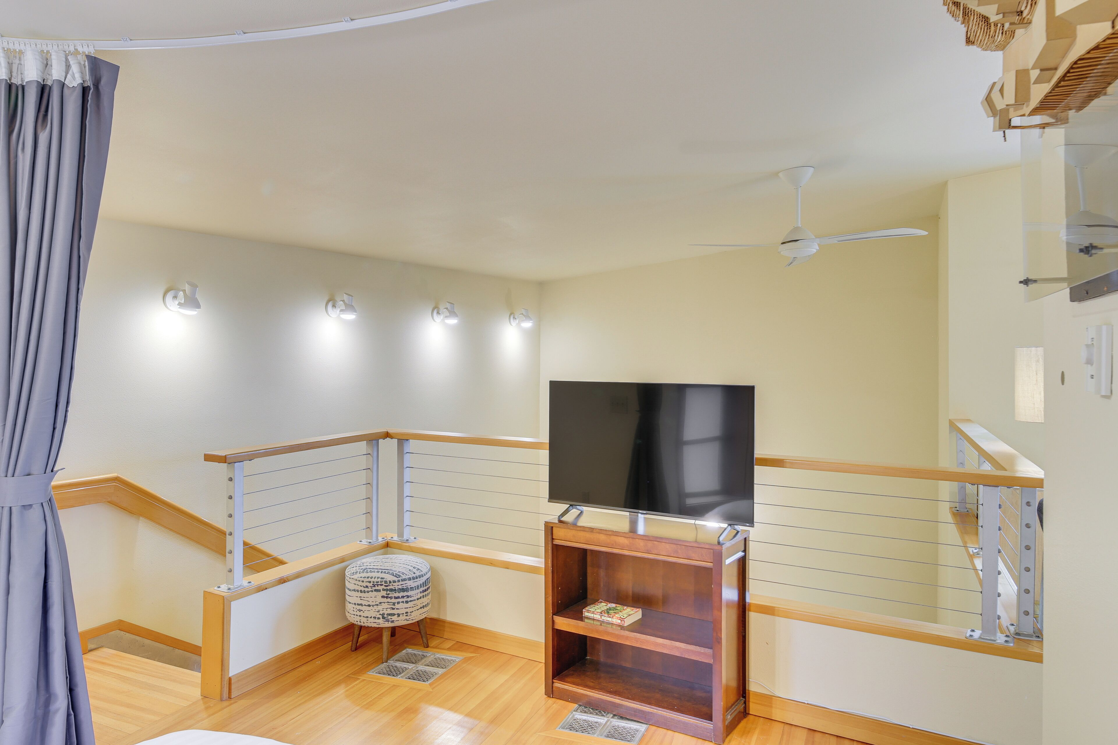 A modern living room with a flat-screen TV, wooden flooring, a ceiling fan, and a staircase with a railing.