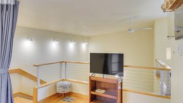 A modern living room with a flat-screen TV, wooden flooring, a ceiling fan, and a staircase with a railing.