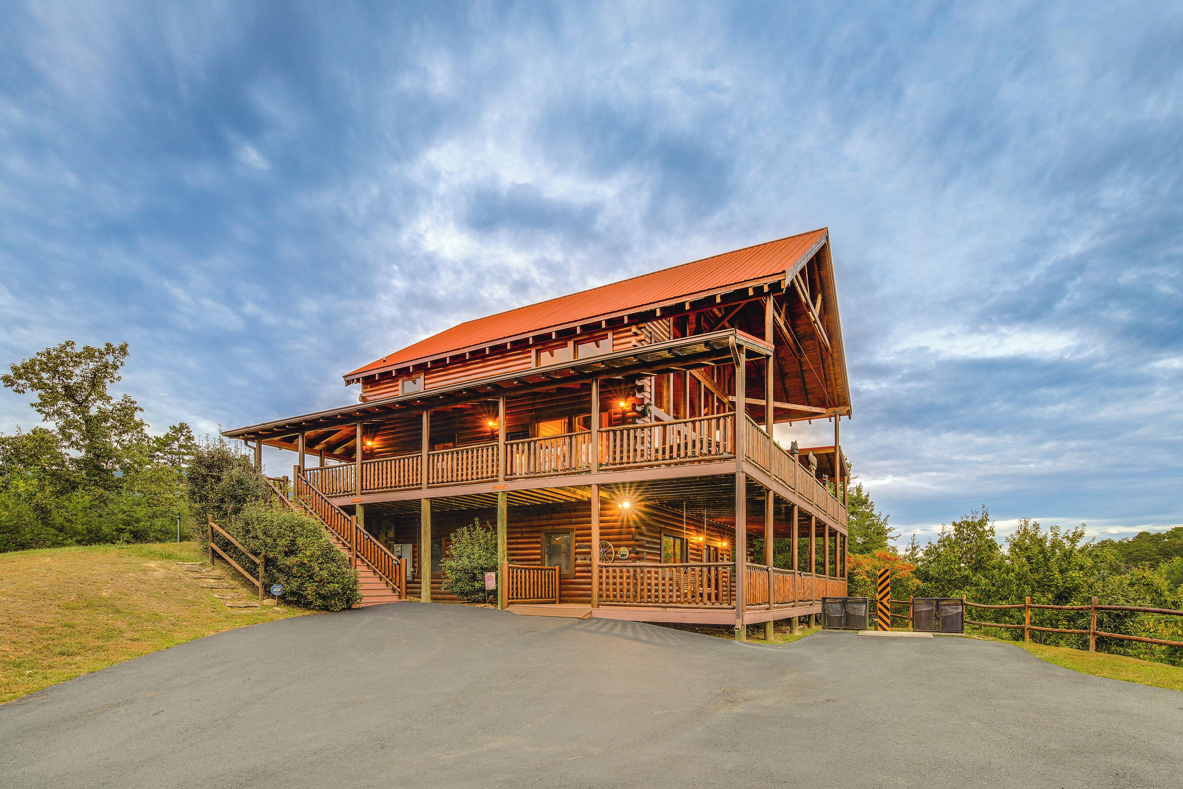 A two-story log cabin with a balcony and a porch, surrounded by a grassy area and trees.