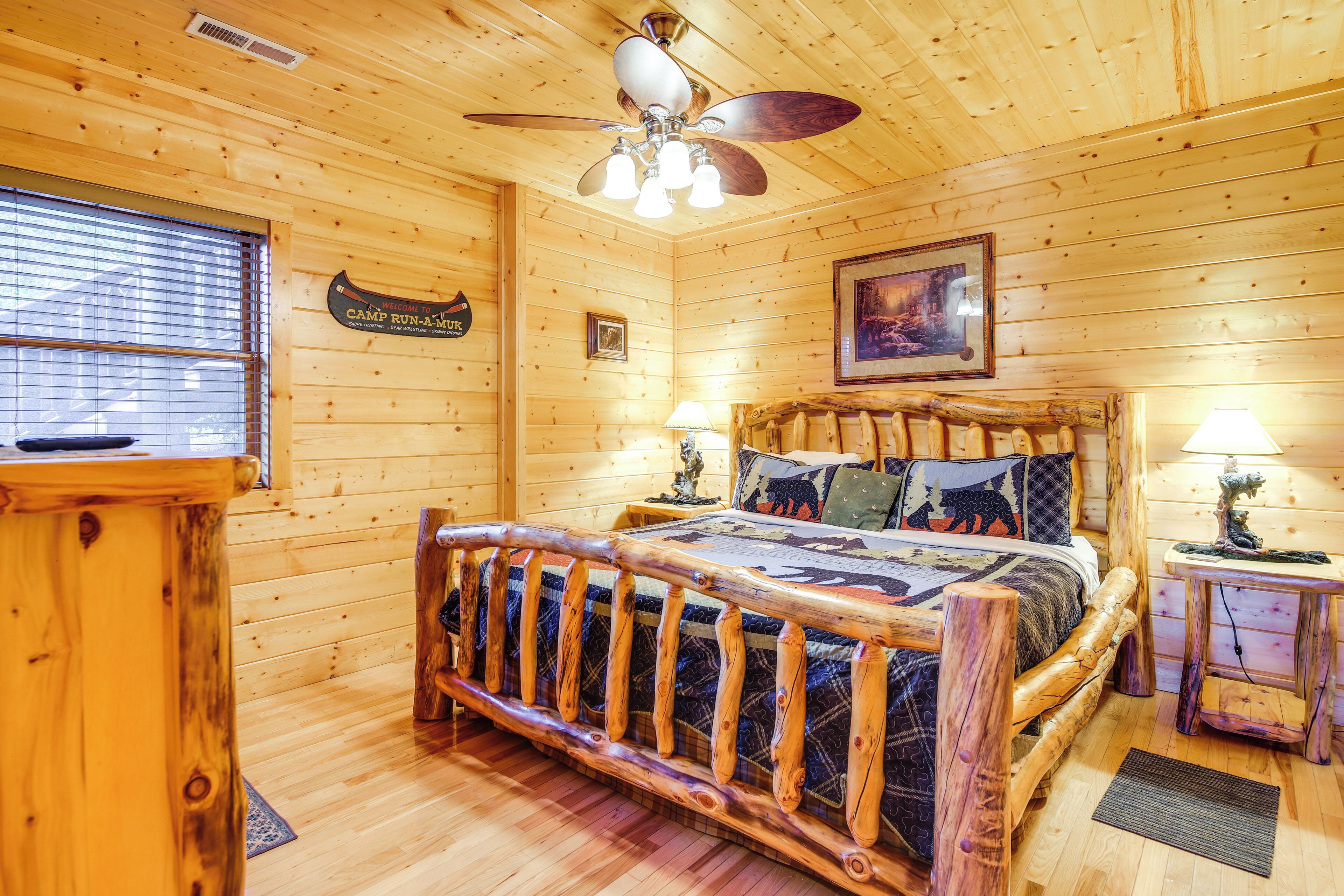 Ein Zimmer in einer Holzhütte mit einem Bett, zwei Nachttischen, einem Deckenventilator und einem Fenster mit Jalousien.
