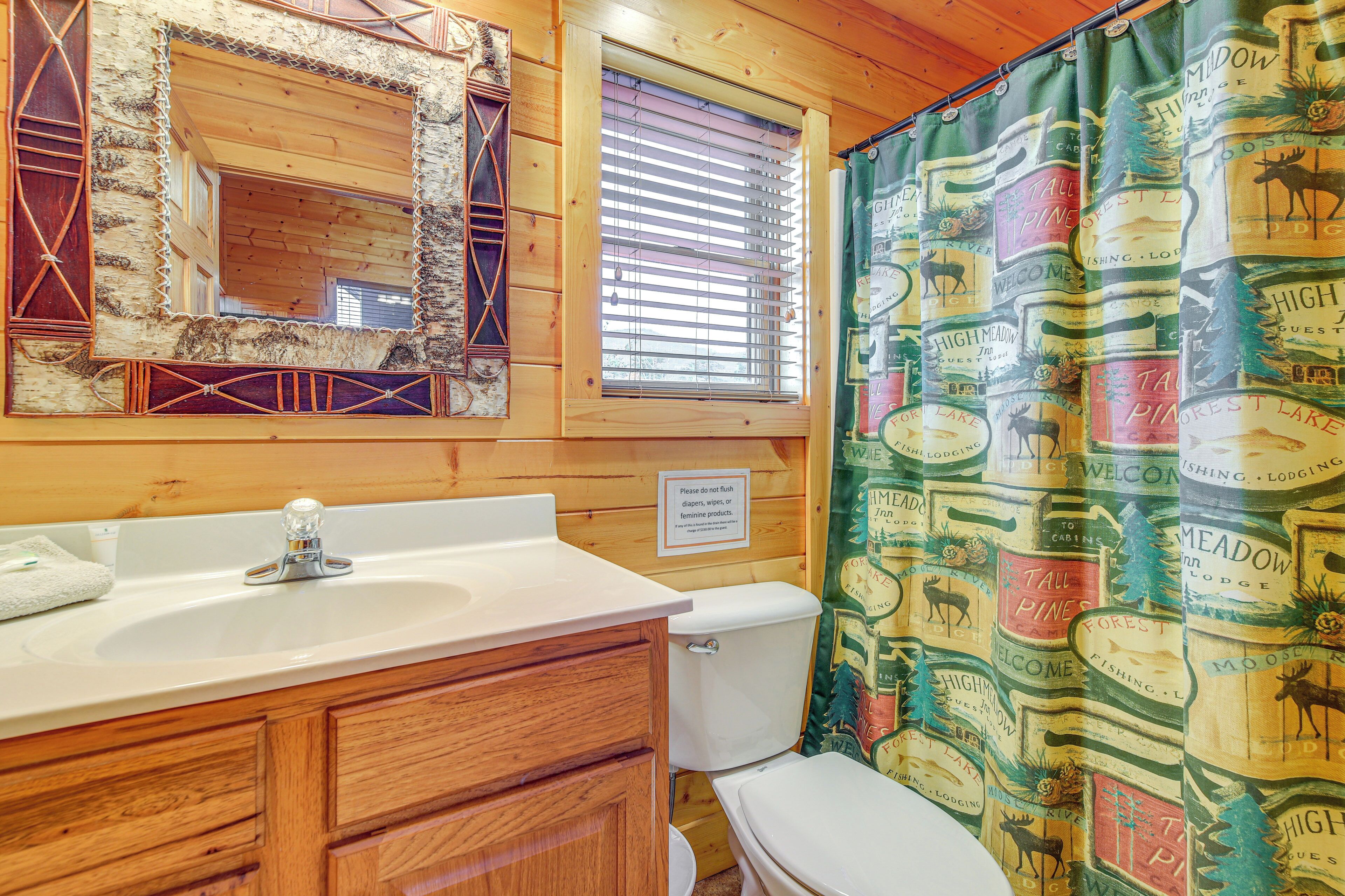 A bathroom with a wooden vanity, a sink, a toilet, and a shower curtain with a forest theme.