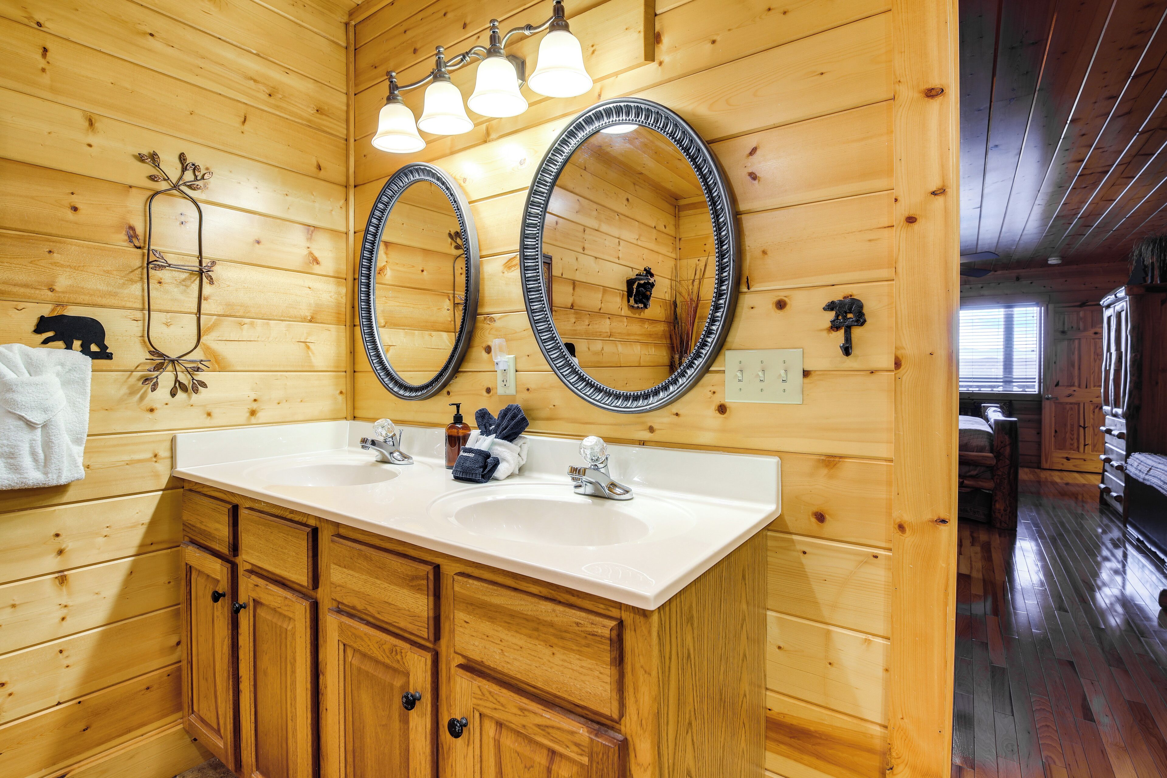 A wooden cabin bathroom with two sinks, wooden cabinets, and a large mirror with a decorative frame.
