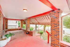 Uma área externa coberta com pilares de tijolo, telhado vermelho e piso de concreto.